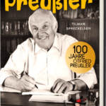 Das Buchcover zeigt Otfried Preußler lächelnd am Schreibtisch, umgeben von Büchern, und ein kleiner, gefiederter Holzspecht steht unten rechts. Die Farben sind warm und einladend.