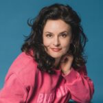 1: Angela Ascher als Kopfportrait vor blauem Hintergrund.