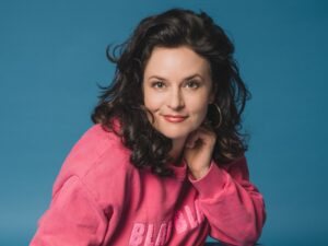 1: Angela Ascher als Kopfportrait vor blauem Hintergrund.