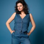 3: Angela Ascher in Jeansweste und -hose vor blauem Hintergrund.