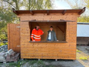 Mitarbeiter des Bauhofs und eine Mitarbeiterin der Tourist‑Info stehen in einer reparierten Weihnachtsmarkthütte.