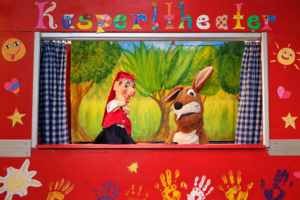 Kasperl und Mucki vor der roten Bühnenkulisse mit Kinderhandabdrücken.