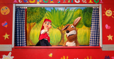 Kasperl und Mucki vor der roten Bühnenkulisse mit Kinderhandabdrücken.