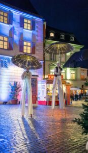 Stelzenläufer mit leuchtenden Regenschirmen bei den "Rosigen Zeiten" in der Rosenheimer Innenstadt.