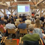 Blick in den Veranstaltungsraum mit Publikum und Vortrag.