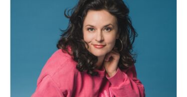 1: Angela Ascher als Kopfportrait vor blauem Hintergrund.