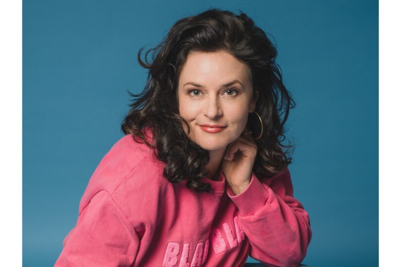 1: Angela Ascher als Kopfportrait vor blauem Hintergrund.