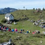 Panoramablick auf die Eggenalm mit Gottesdienstbesuchern und Alphornbläsern