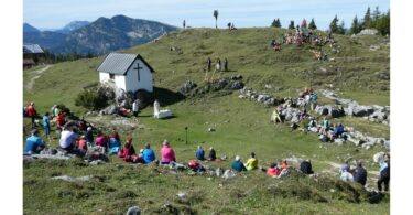 Panoramablick auf die Eggenalm mit Gottesdienstbesuchern und Alphornbläsern
