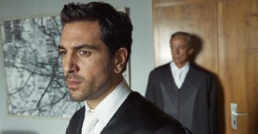 Szene aus 'Der Fall Collini' mit einem jungen Anwalt im Vordergrund.