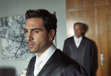 Szene aus 'Der Fall Collini' mit einem jungen Anwalt im Vordergrund.