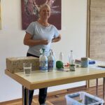 1: Vortragende stellt EM-Produkte auf einem Tisch vor