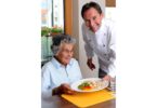 Koch serviert einer Seniorin ein Essen in einer Einrichtung