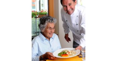 Koch serviert einer Seniorin ein Essen in einer Einrichtung