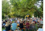 Gut besuchter Biergarten mit Gästen und Musik unter Bäumen