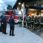 Schiedsrichter und Feuerwehrleute vor dem Feuerwehrhaus und Löschfahrzeug.