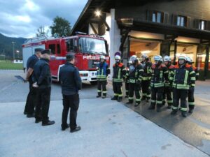Schiedsrichter und Feuerwehrleute vor dem Feuerwehrhaus und Löschfahrzeug.