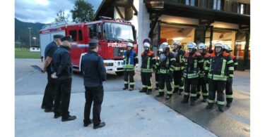 Schiedsrichter und Feuerwehrleute vor dem Feuerwehrhaus und Löschfahrzeug.