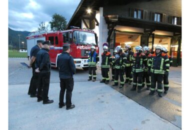 Schiedsrichter und Feuerwehrleute vor dem Feuerwehrhaus und Löschfahrzeug.