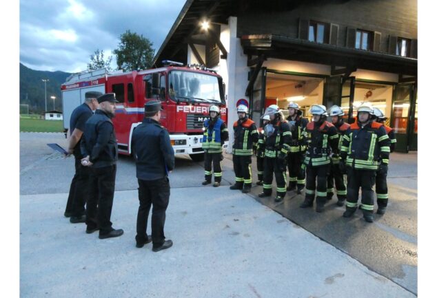 Schiedsrichter und Feuerwehrleute vor dem Feuerwehrhaus und Löschfahrzeug.