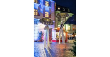 Stelzenläufer mit leuchtenden Regenschirmen bei den "Rosigen Zeiten" in der Rosenheimer Innenstadt.