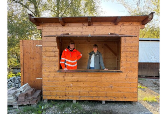 Mitarbeiter des Bauhofs und eine Mitarbeiterin der Tourist‑Info stehen in einer reparierten Weihnachtsmarkthütte.