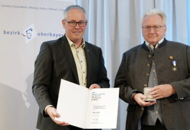 Zwei Männer sind festlich gekleidet. Sie halten Urkunde und Medaille in den Händen.