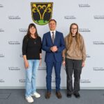 Drei Personen stehen vor einer Wand mit dem Schriftzug der Großen Kreisstadt Traunstein.