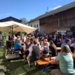 Besucher beim Kirtafest sitzen an Bänken im Freien.