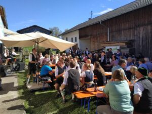 Besucher beim Kirtafest sitzen an Bänken im Freien.