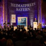 Bühne mit Projektion 'Heimatpreis Bayern' und einem Redner am Podium.