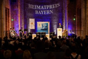 Bühne mit Projektion 'Heimatpreis Bayern' und einem Redner am Podium.