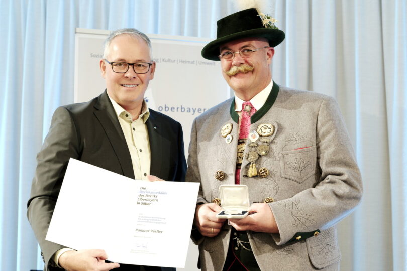 Zwei Männer sind festlich gekleidet. Sie halten Urkunde und Medaille in den Händen.
