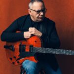 Bireli Lagrene mit Gitarre vor rotem Hintergrund.