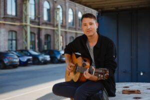 Daniel Stelter spielt Gitarre vor einem Backsteingebäude.