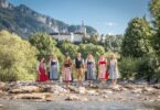 Das Team der Tourist Info Aschau und Sachrang am Ufer vor den Bergen.