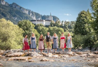 Das Team der Tourist Info Aschau und Sachrang am Ufer vor den Bergen.