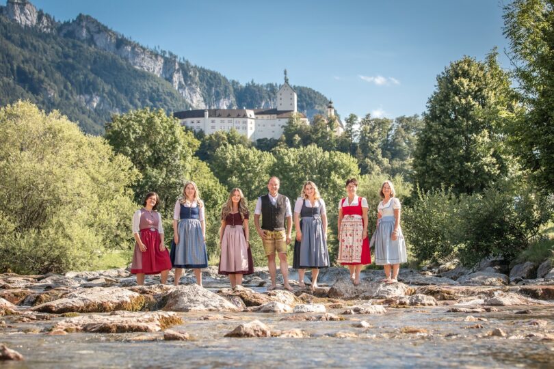 Das Team der Tourist Info Aschau und Sachrang am Ufer vor den Bergen.