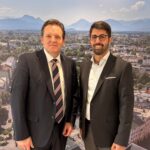 René Zumtobel und Abuzar Erdogan im Rathausfoyer vor einem Panoramabild von Rosenheim.