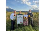 Personen mit Sonnenblumen neben einem Schild 'Blühender Acker für mehr Artenvielfalt'.