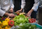 Köche richten Speisen an, frisches Gemüse liegt im Vordergrund.