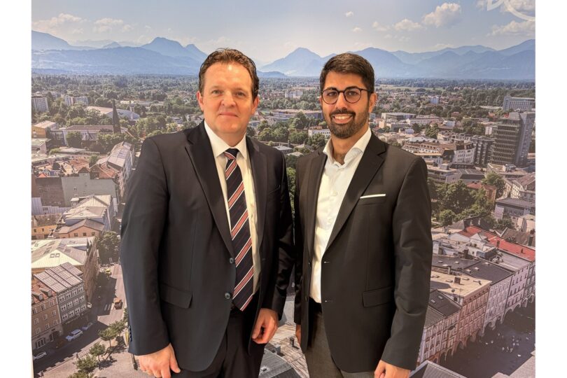 René Zumtobel und Abuzar Erdogan im Rathausfoyer vor einem Panoramabild von Rosenheim.